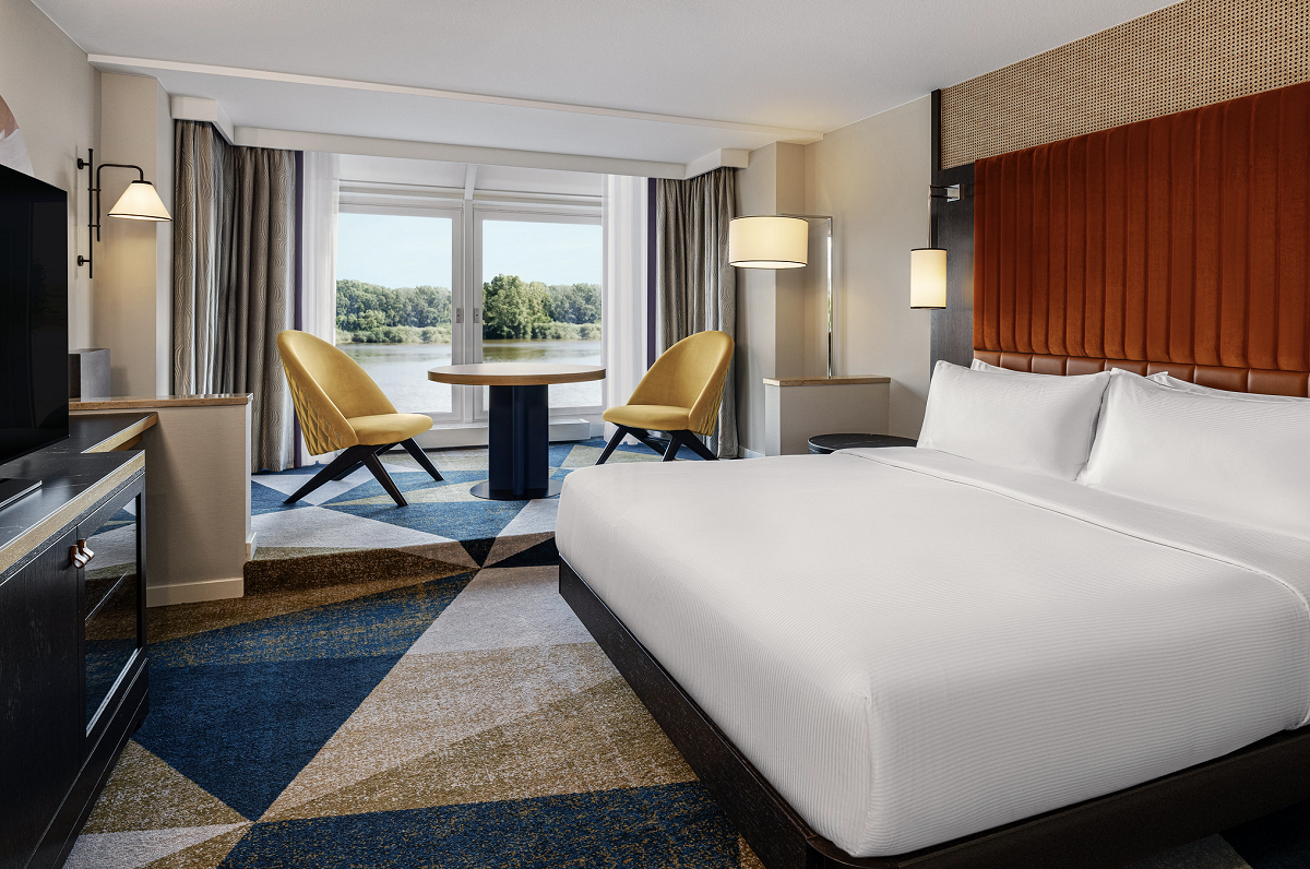 geometric patterned carpet and bed against rust headboard in guestroom with river view