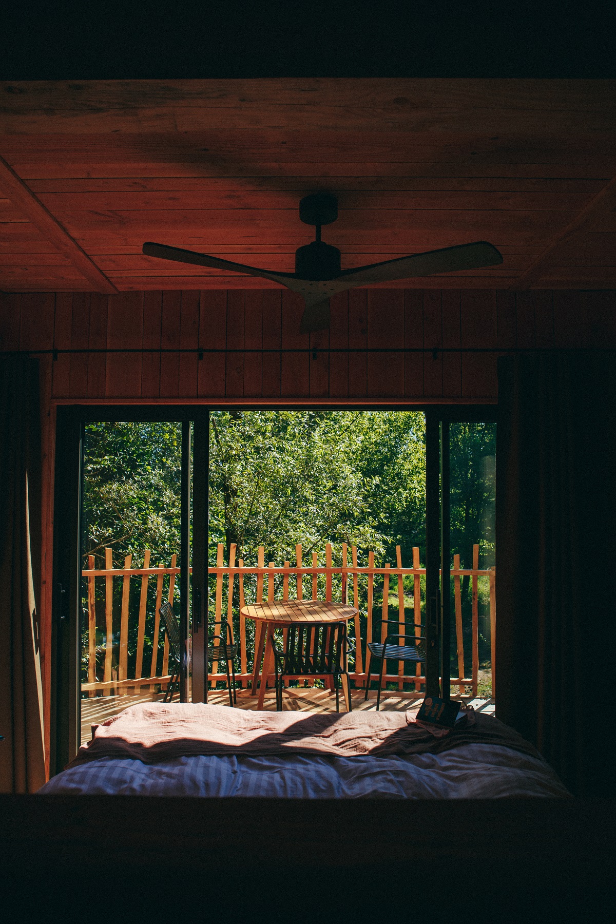 view from cabin bed with ceiling fan looking across treetops 