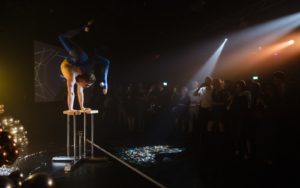 Hand balance act lit up on stage with crowd in the background