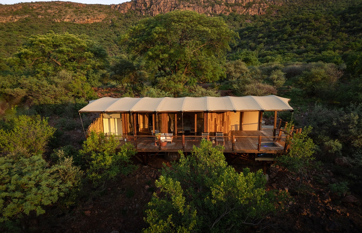 exterior view of safari lodge with tented roof amongst canopy of trees