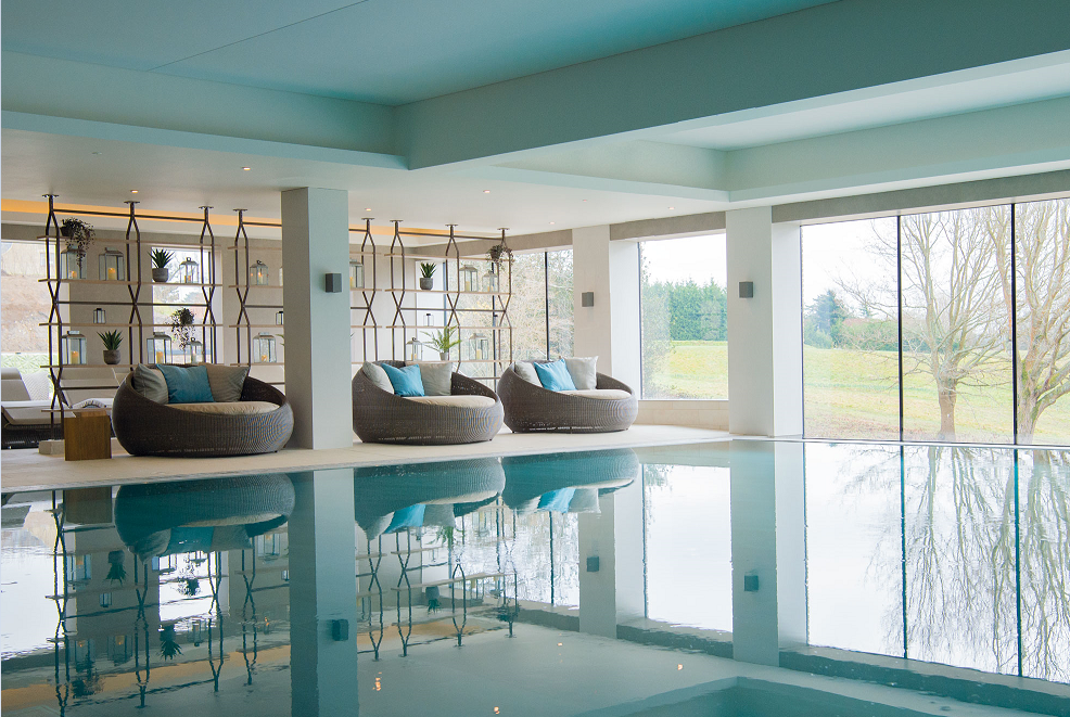 indoor swimming pool and spa in blue and grey with seats looking out of floor to ceiling windows