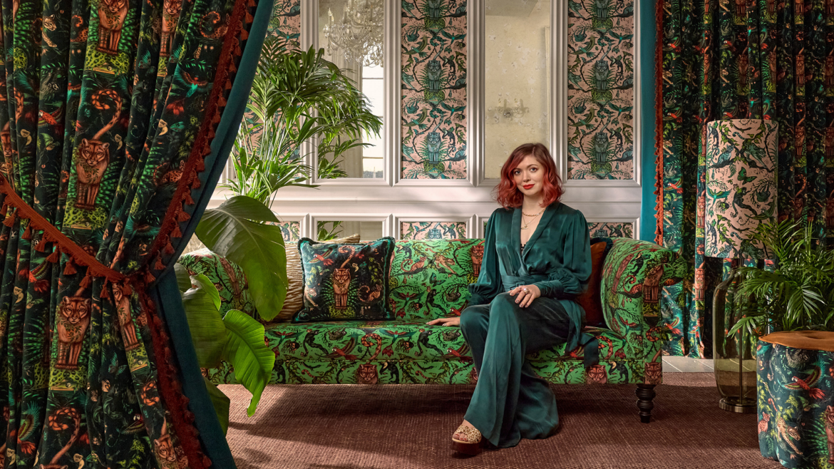 artist emma shipley on a green velvet couch with patterned drapes from Mythica collection