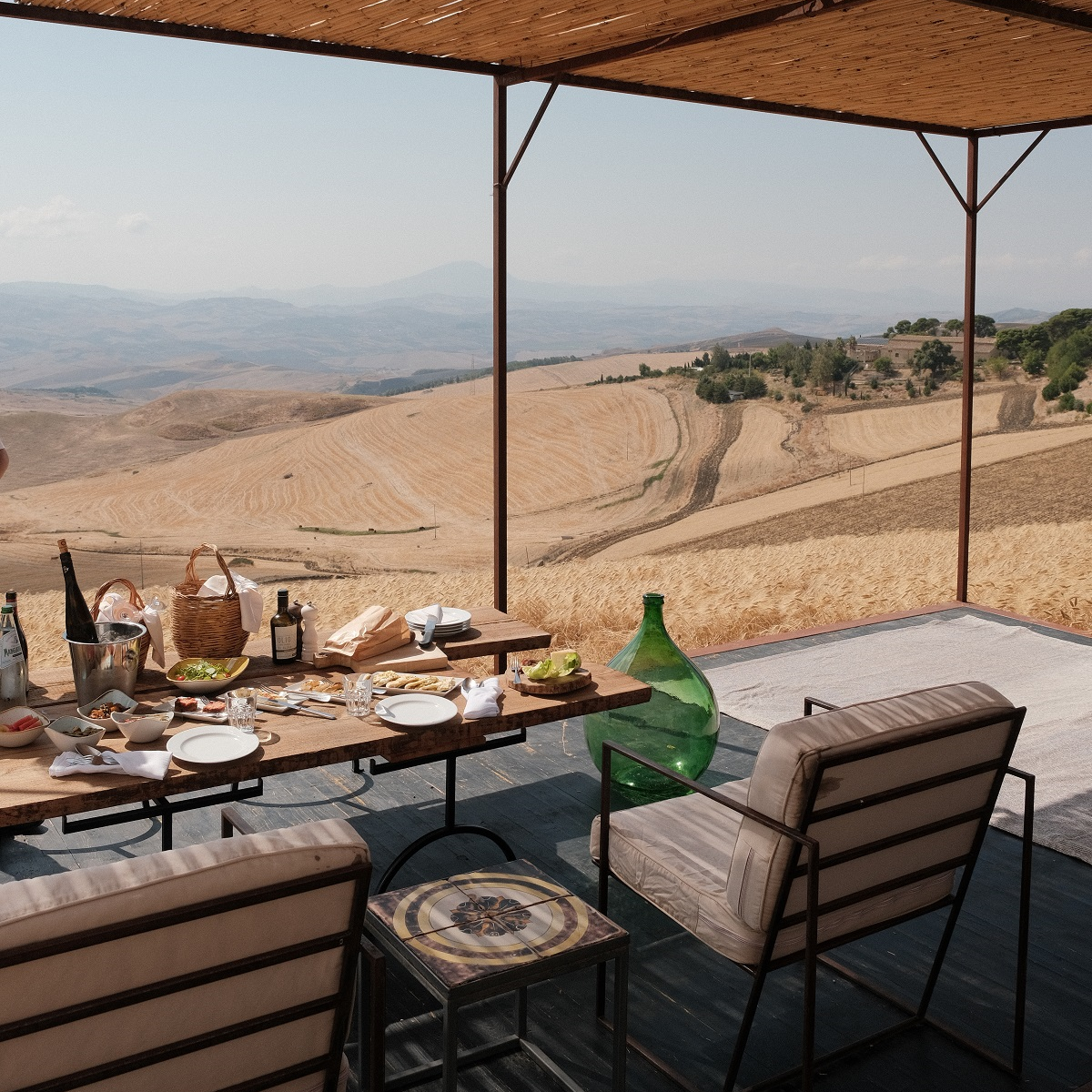 outdoor dining table under bamboo roof with views across sicilian countryside