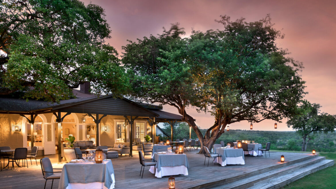 andBeyond Kirkmans Kamp, outside restaurant surrounded by trees with a pink sunset sky