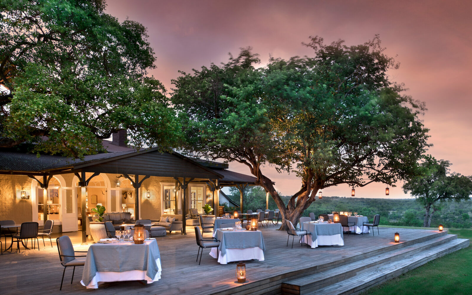 andBeyond Kirkmans Kamp, outside restaurant surrounded by trees with a pink sunset sky