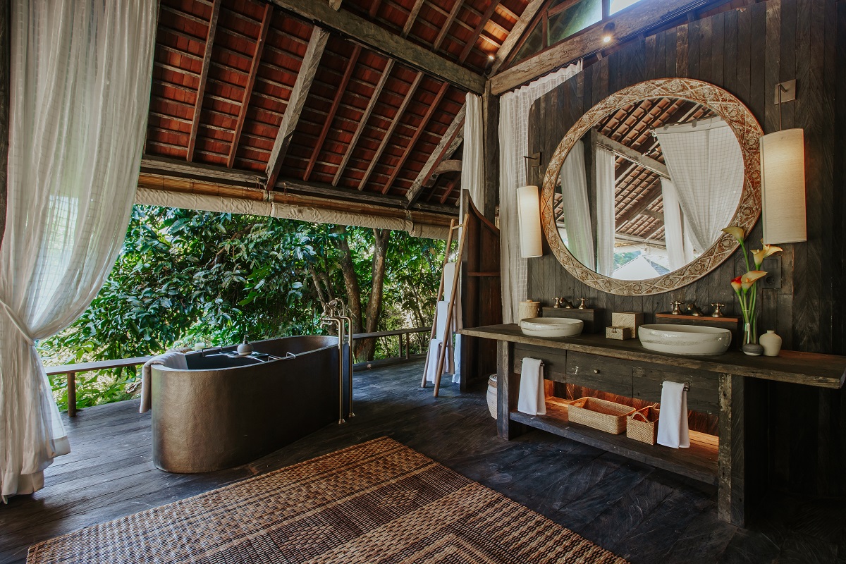 Open air bathroom in the jungle, with wooden floor and dark stone bath.