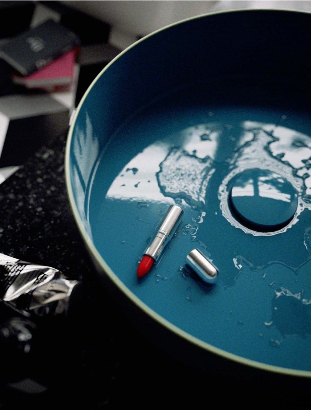 Teal colourway of Alape's new tricolour washbasin design, shown with water splatter and a unlidded red lipstick in basin