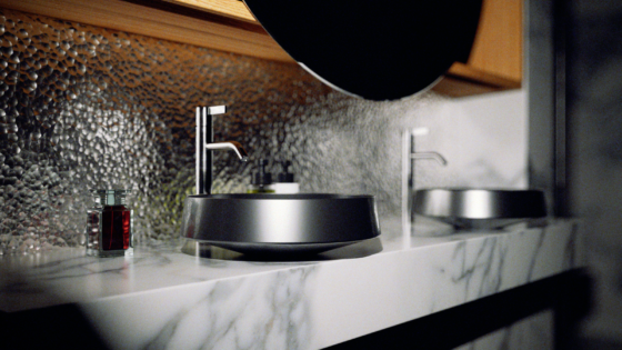 Alape washbasin in steel finish, on grey and white marble countertop with hammered silver metal splashback