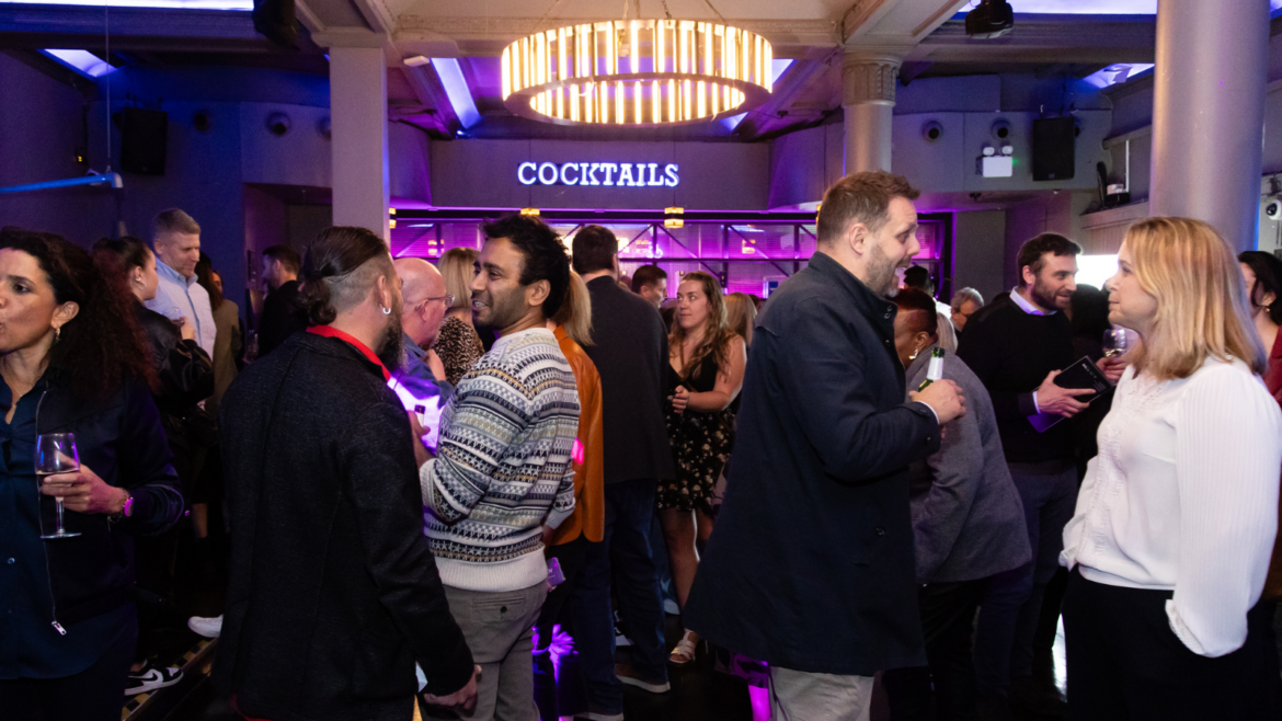Group of MEET UP London attendees stood infront of neon lit cocktail sign and bar