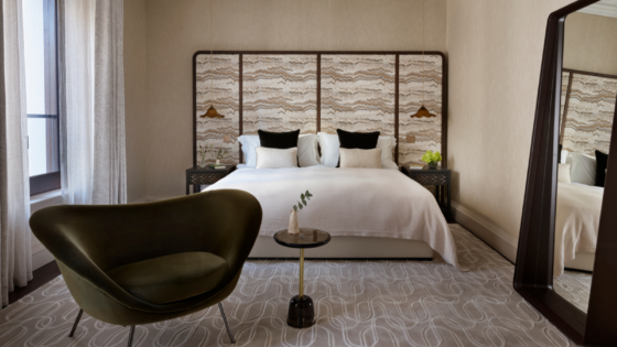 Neutral-toned bedroom, mid-century modernism in design, in The OWO Residences by Raffles. Textured headboard frames the bed, while a tall mirror leans against the wall to the right and a organic shaped armchair sits to the left of the bed. By StudioMorey