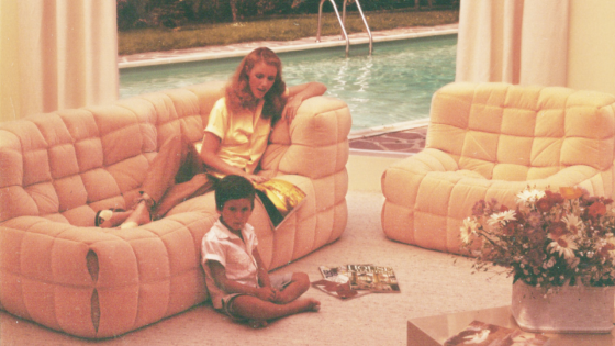 pastel-hued photograph of mother laying on a Kashima sofa by Ligne Roset, with child reading magazine on floor beside her