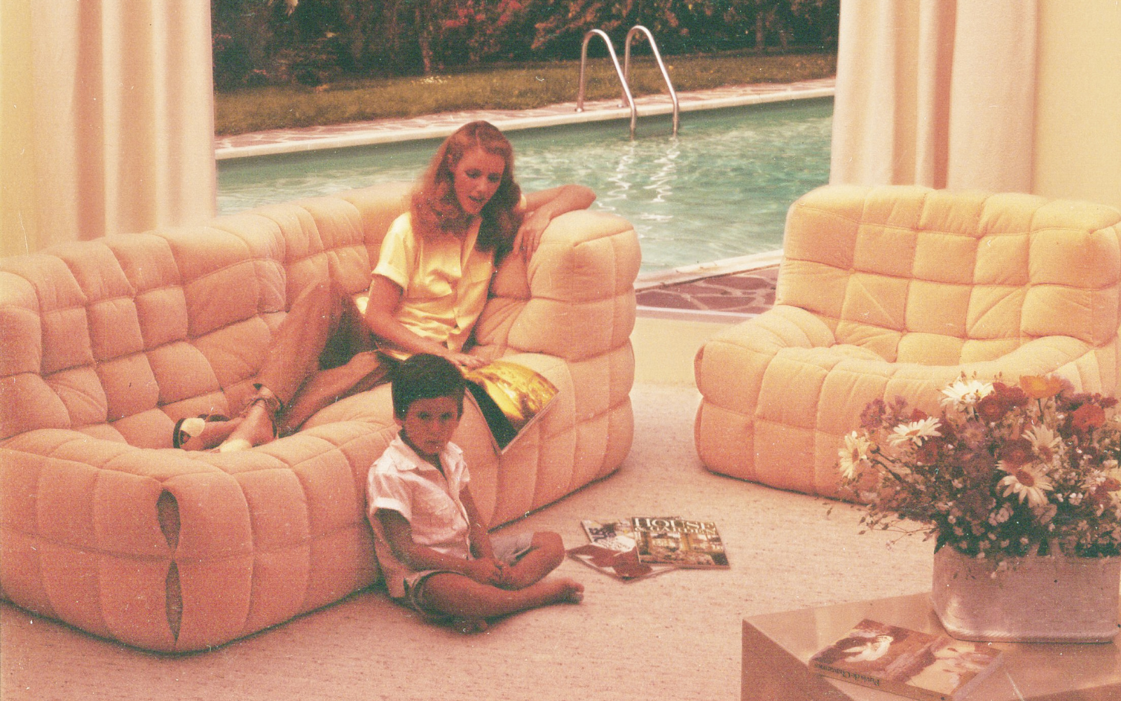 pastel-hued photograph of mother laying on a Kashima sofa by Ligne Roset, with child reading magazine on floor beside her