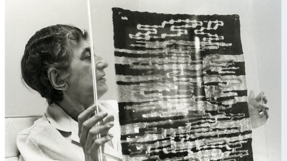 Black and white image of artists Anni Albers, holding a textile piece of artwork