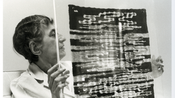 Black and white image of artists Anni Albers, holding a textile piece of artwork