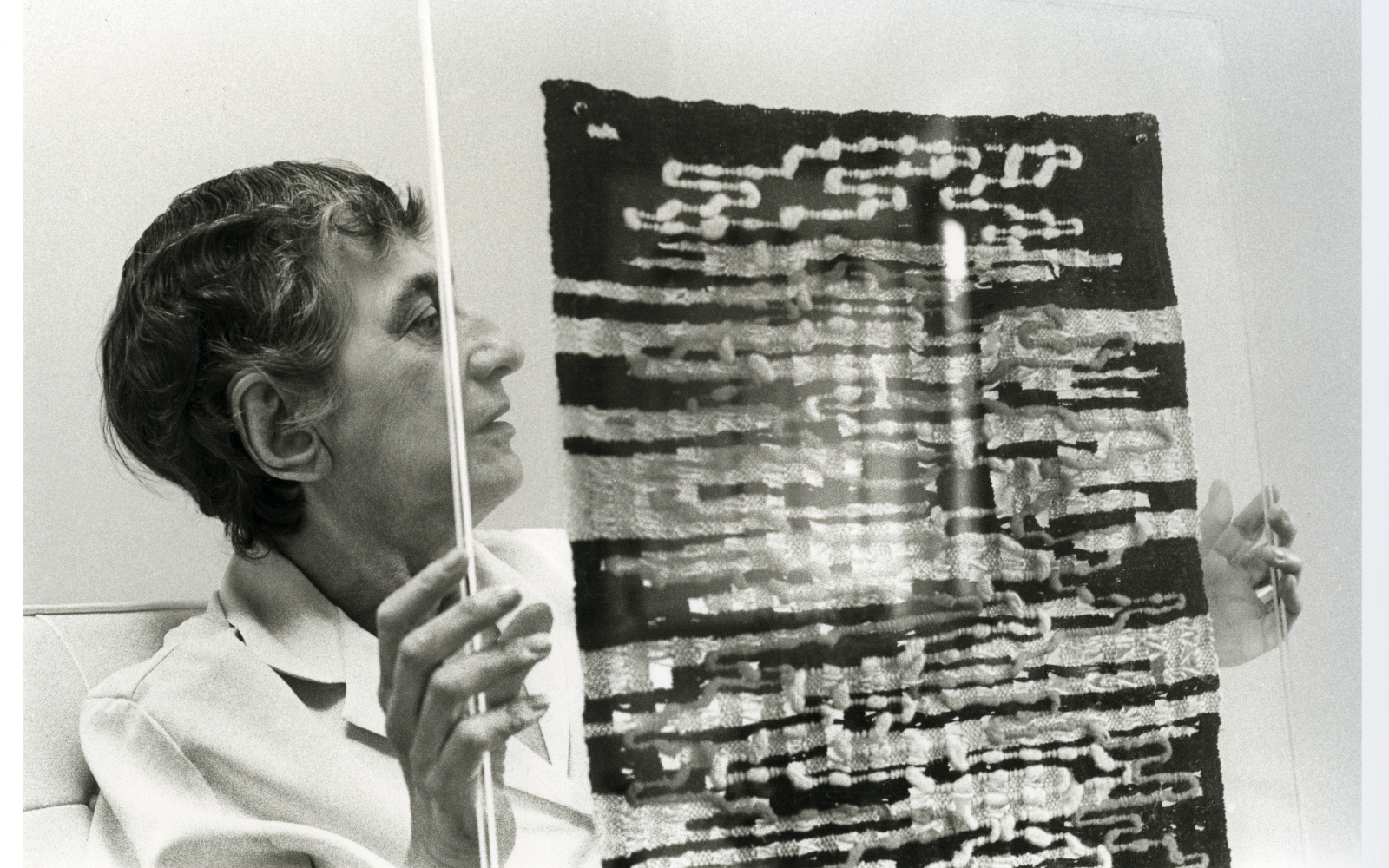 Black and white image of artists Anni Albers, holding a textile piece of artwork