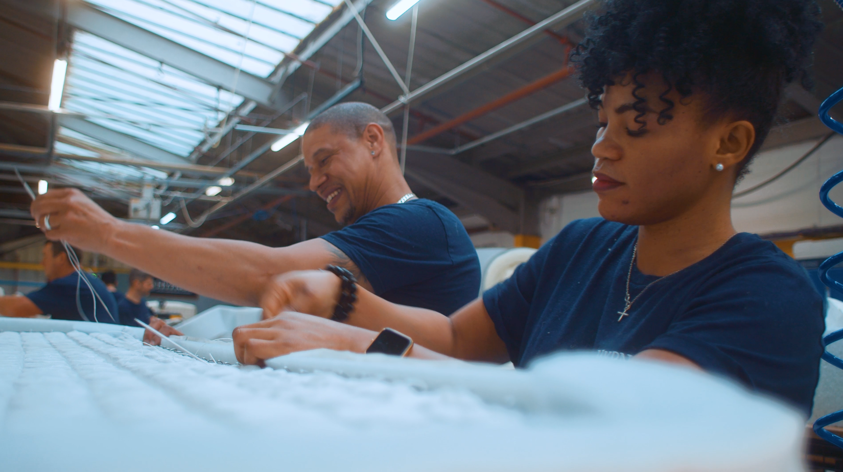 Close up shot of man and woman sewing a Hypnos mattress, in the factory