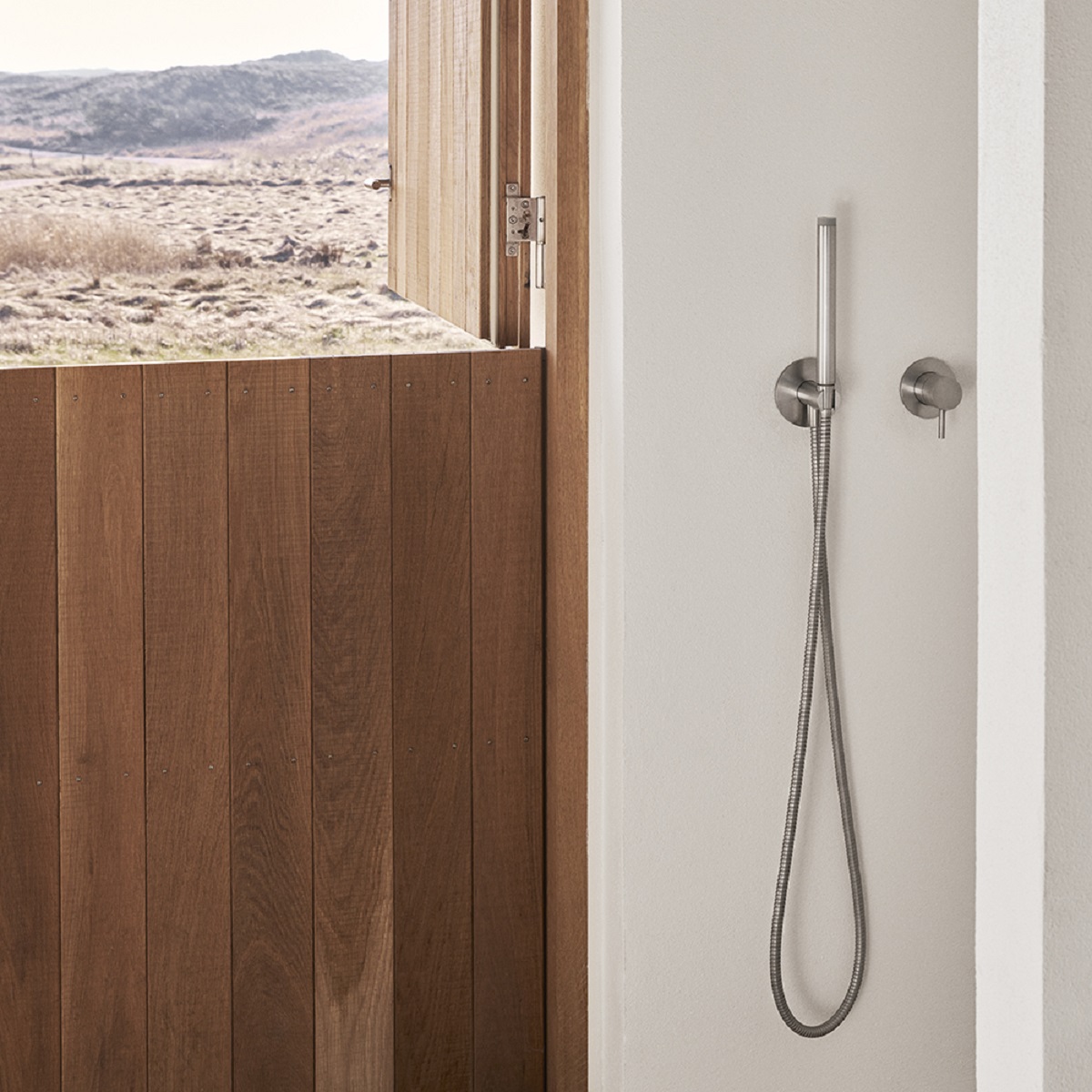 simple wall mounted shower next to open wooden door onto dunes