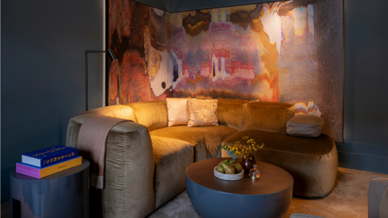 Dark, ashy purple walled seating area at The Rosewood Amsterdam. A multi-coloured watery paint painting hangs behind a mustard toned mid-century design sofa.