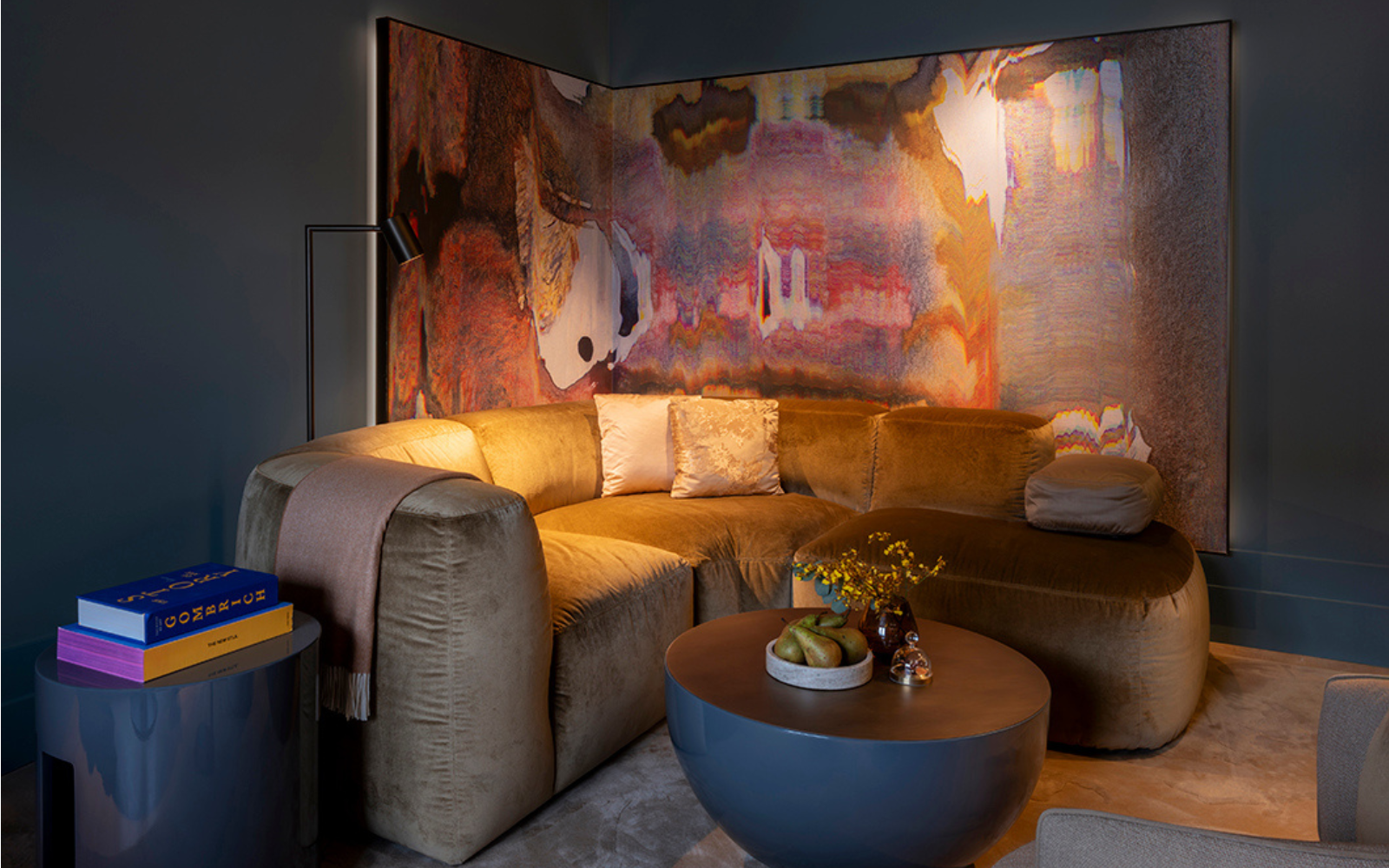 Dark, ashy purple walled seating area at The Rosewood Amsterdam. A multi-coloured watery paint painting hangs behind a mustard toned mid-century design sofa.