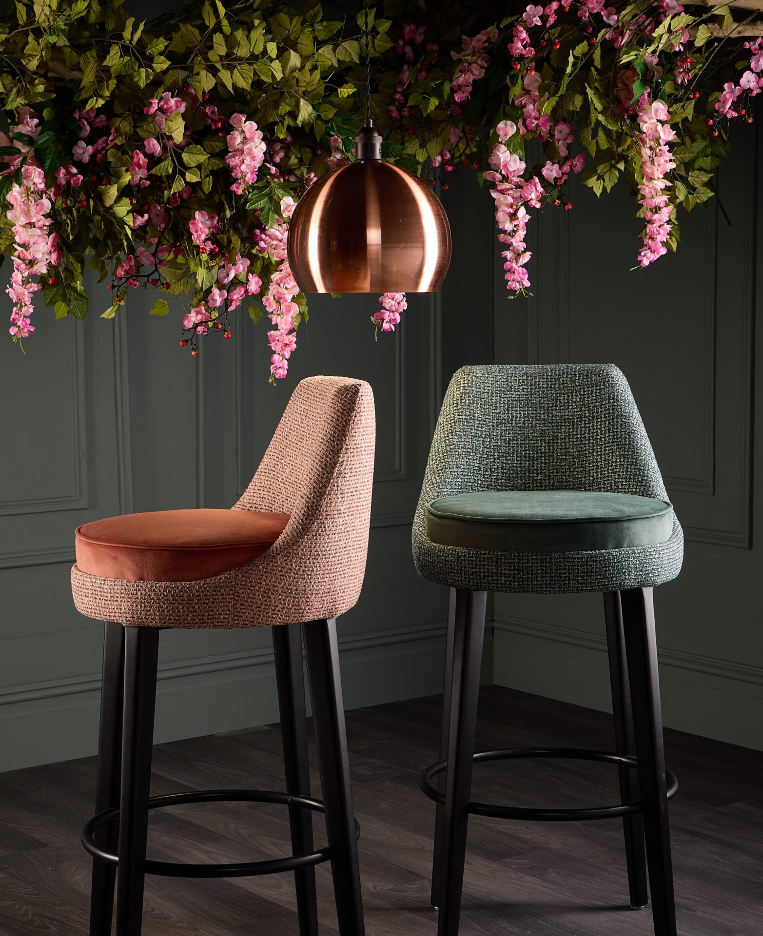 Skopos Esme upholstery fabric in orange and green on dark bar stools with pink flower background