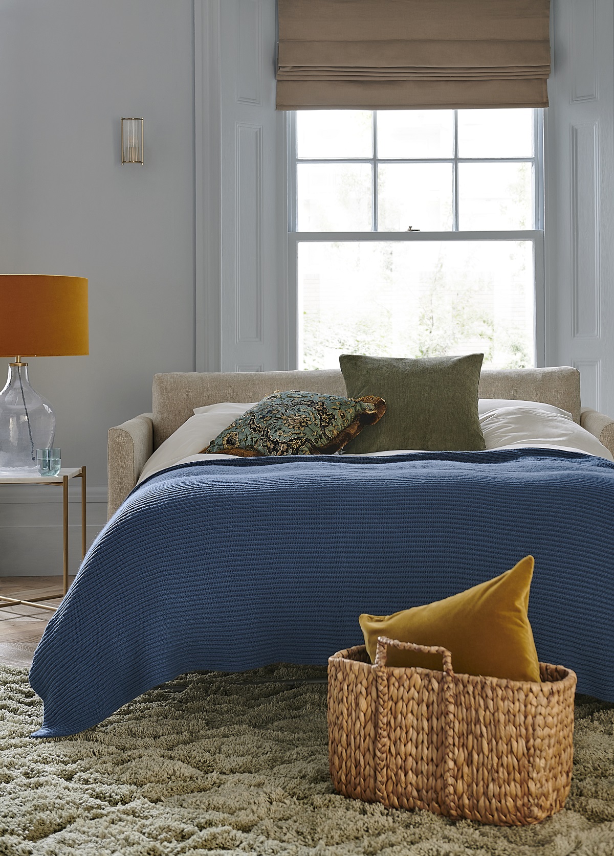 Aissa loveseat sofabed covered in natural coloured norfolk cotton with baskets, textured carpet and blue throw