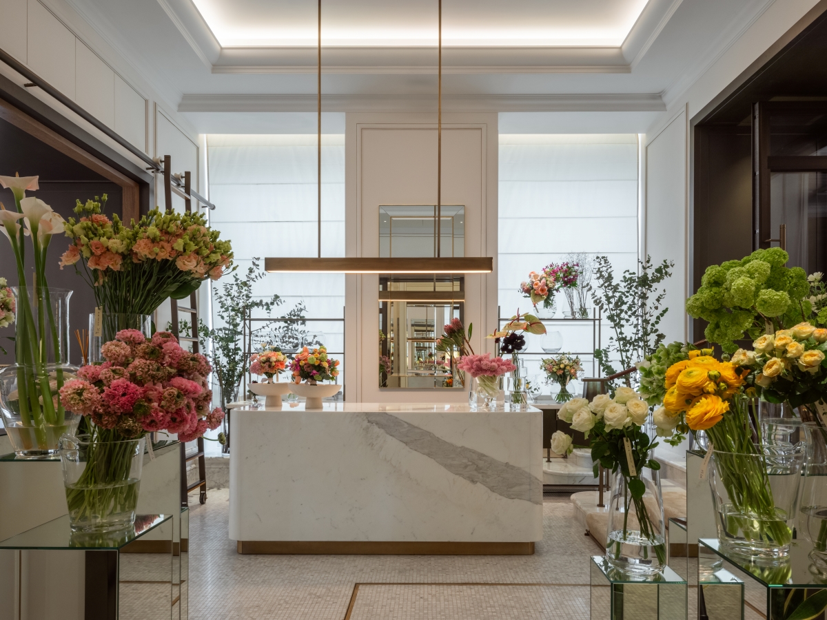 Florist at the Corinthia Bucharest, white walls and marble counter sit central while glass vases filled with brighlty lit flowers line the walkway