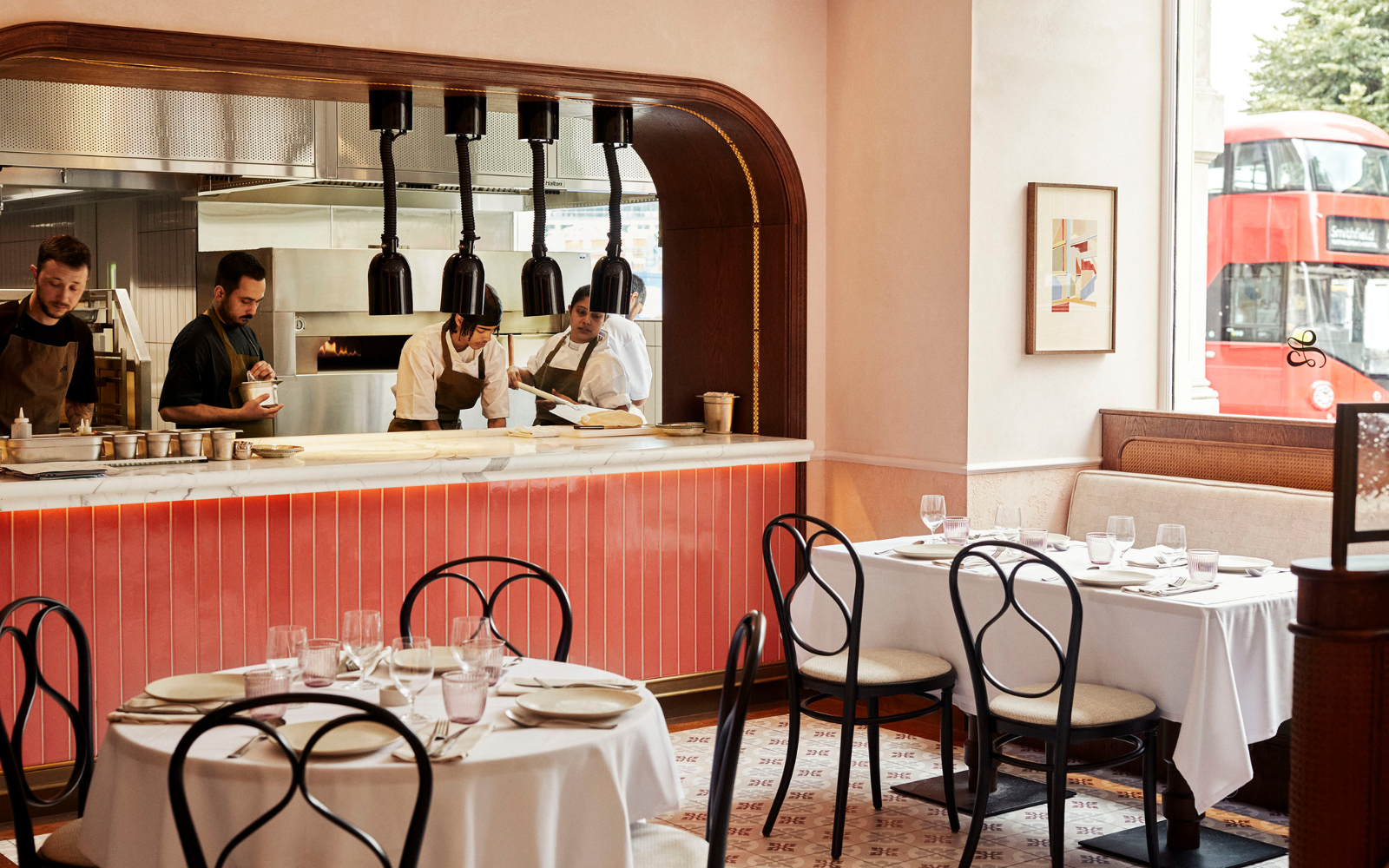Leydi restaurant at Hyde Hotel London, with pink tiled open kitchen and french bistro style chairs around round tables with white table cloth
