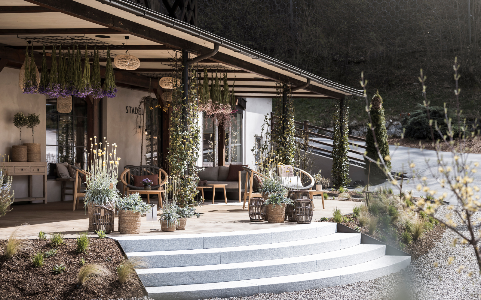 Outside shot of The Barn by NOA, with dried flowers hanging from the veranda rafters and white stone steps down to road