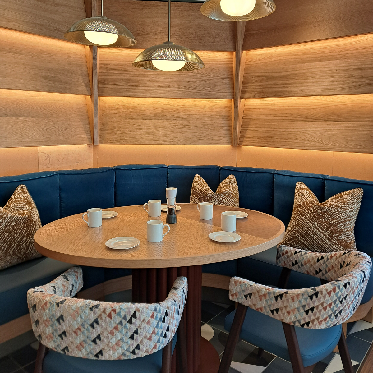 a curved banquette wraps around an oval table, creating a private retreat beneath the soft glow of satin brass pendant lights