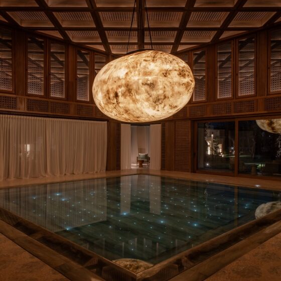 Lit moon installation hanging above starlit pool