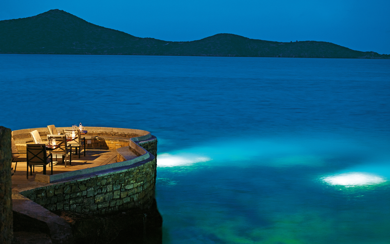 Sumosan restaurant at Elounda Collection, curved stone jetty looks out across ocean at night