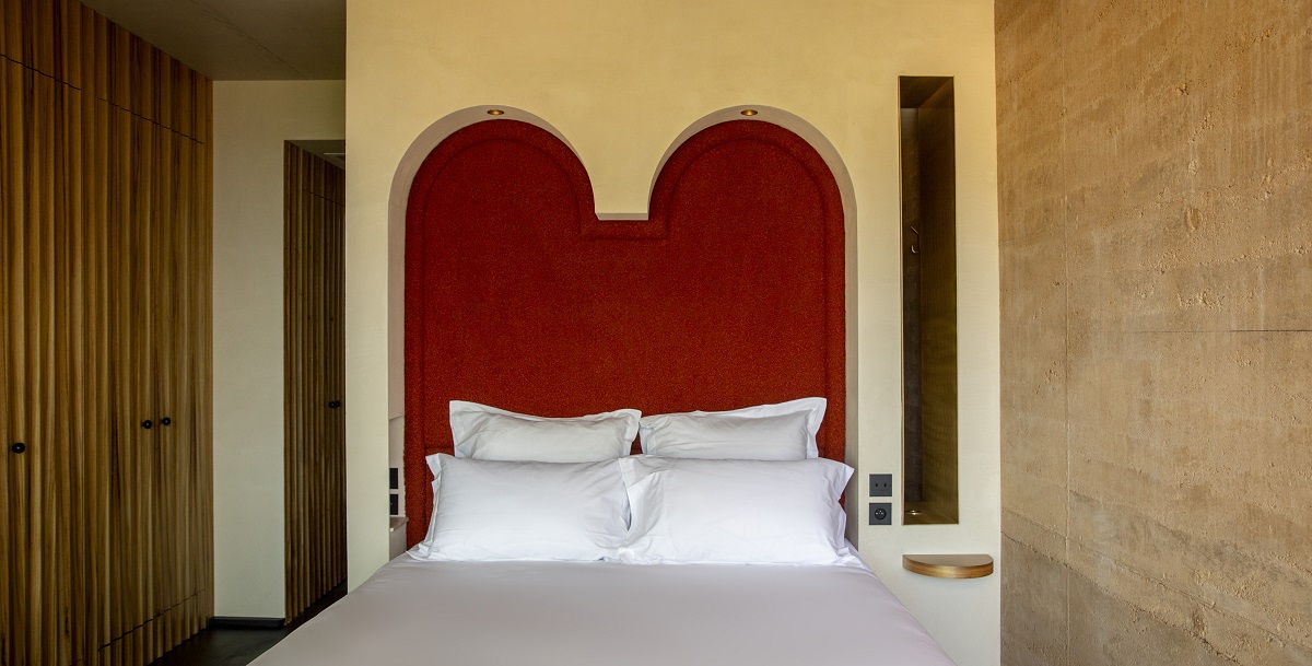 bed with white linen and arched recess bedhead in red against stone wall
