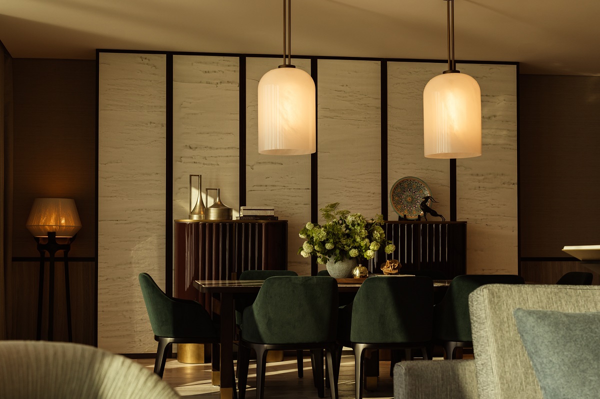 dark wood dining table and green velvet chairs below two pendant lights in suite in Rosewood Doha