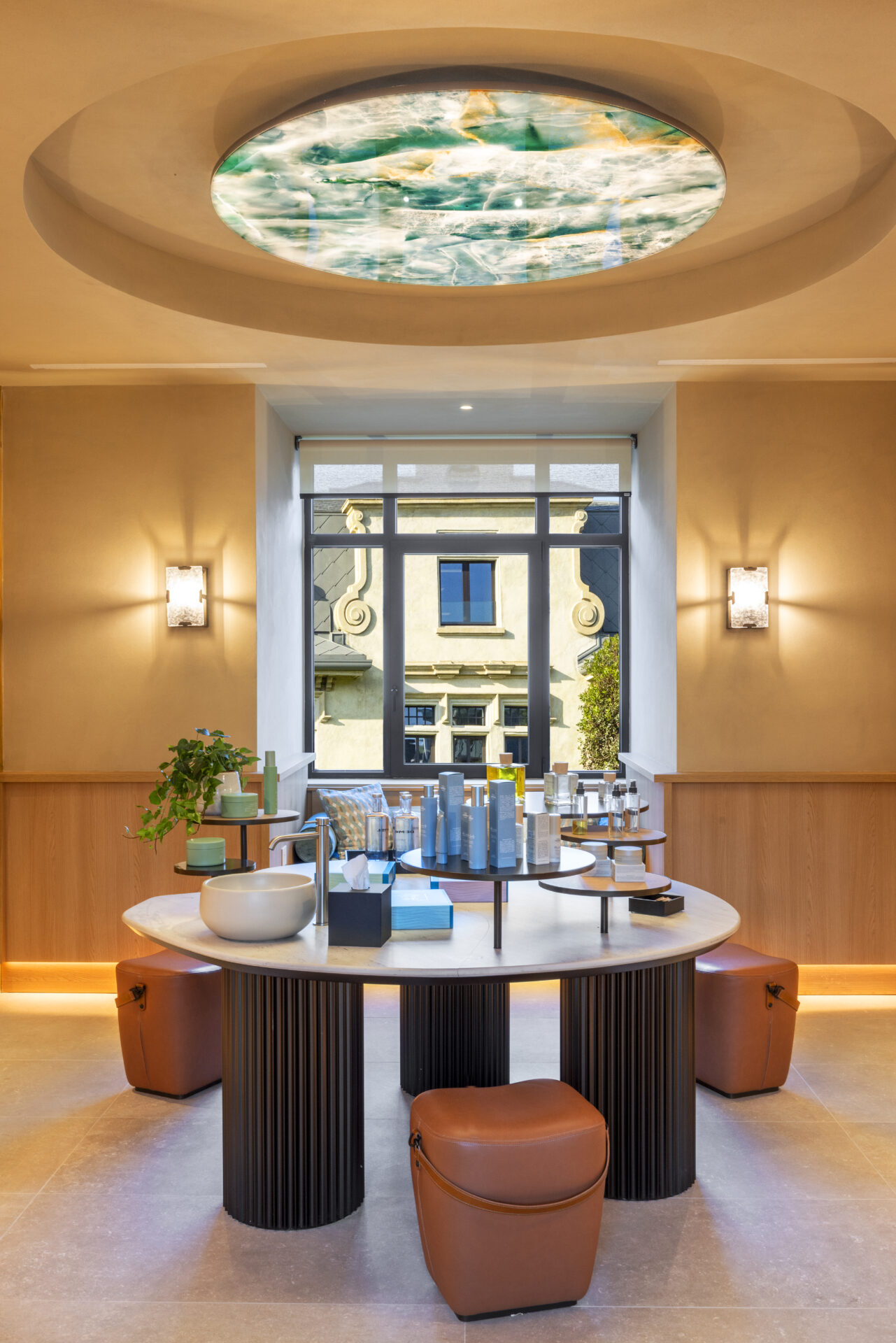 Treatment lobby at De Montel: Terme di Milano, with circular table central and leather stools surrounding. A travertine circle sits on the ceiling above.