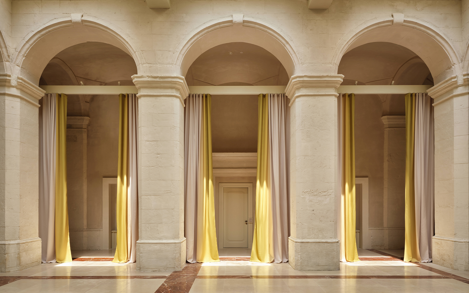 3 arches in cream stone framed with yellow floor to ceiling curtains in Vista Ostuni - a five-star luxury hotel and part of the Vista brand