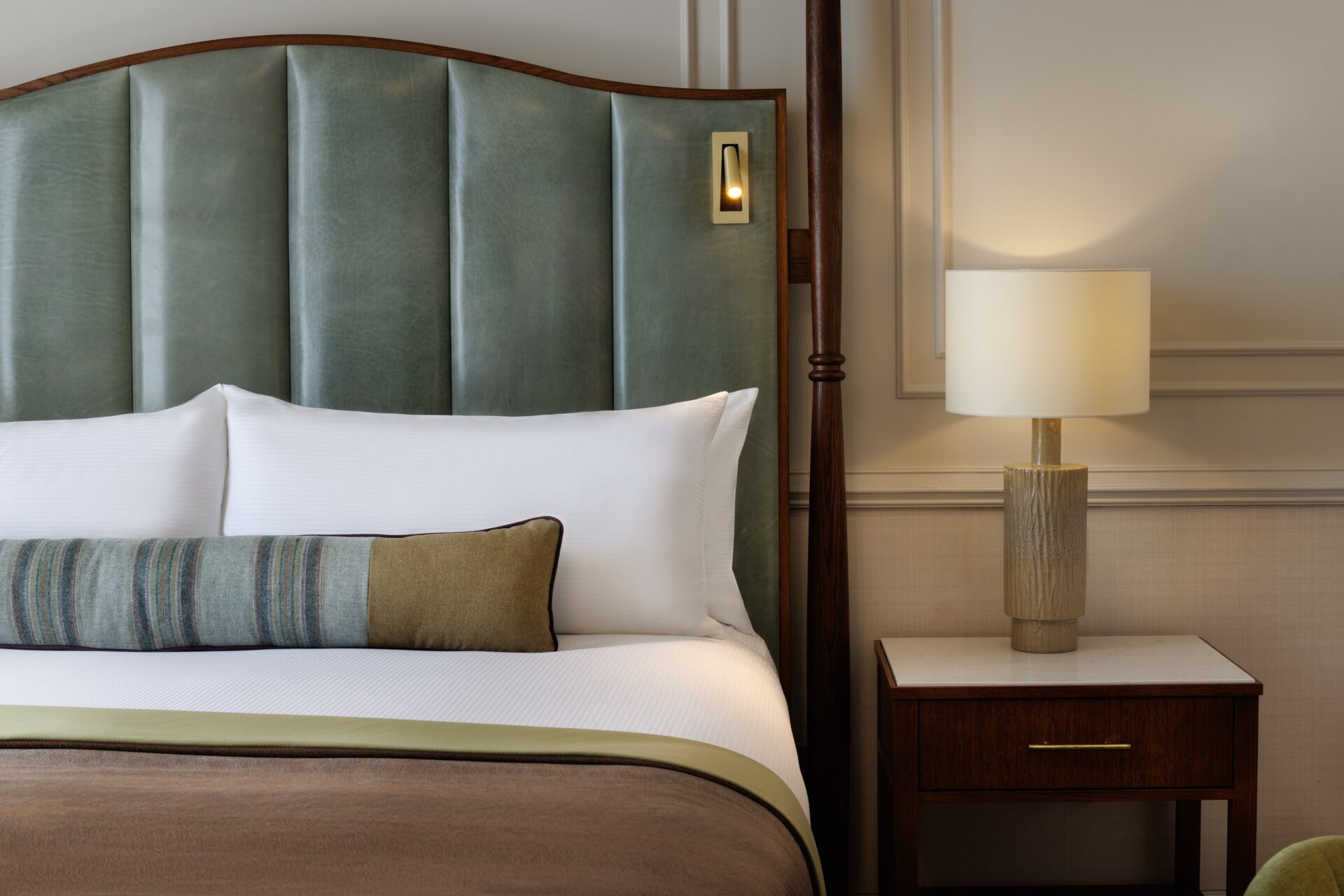 Halsa lamp by Northern Lights: bottle-like base with cream shade, on bedside table besides a green velvet bed