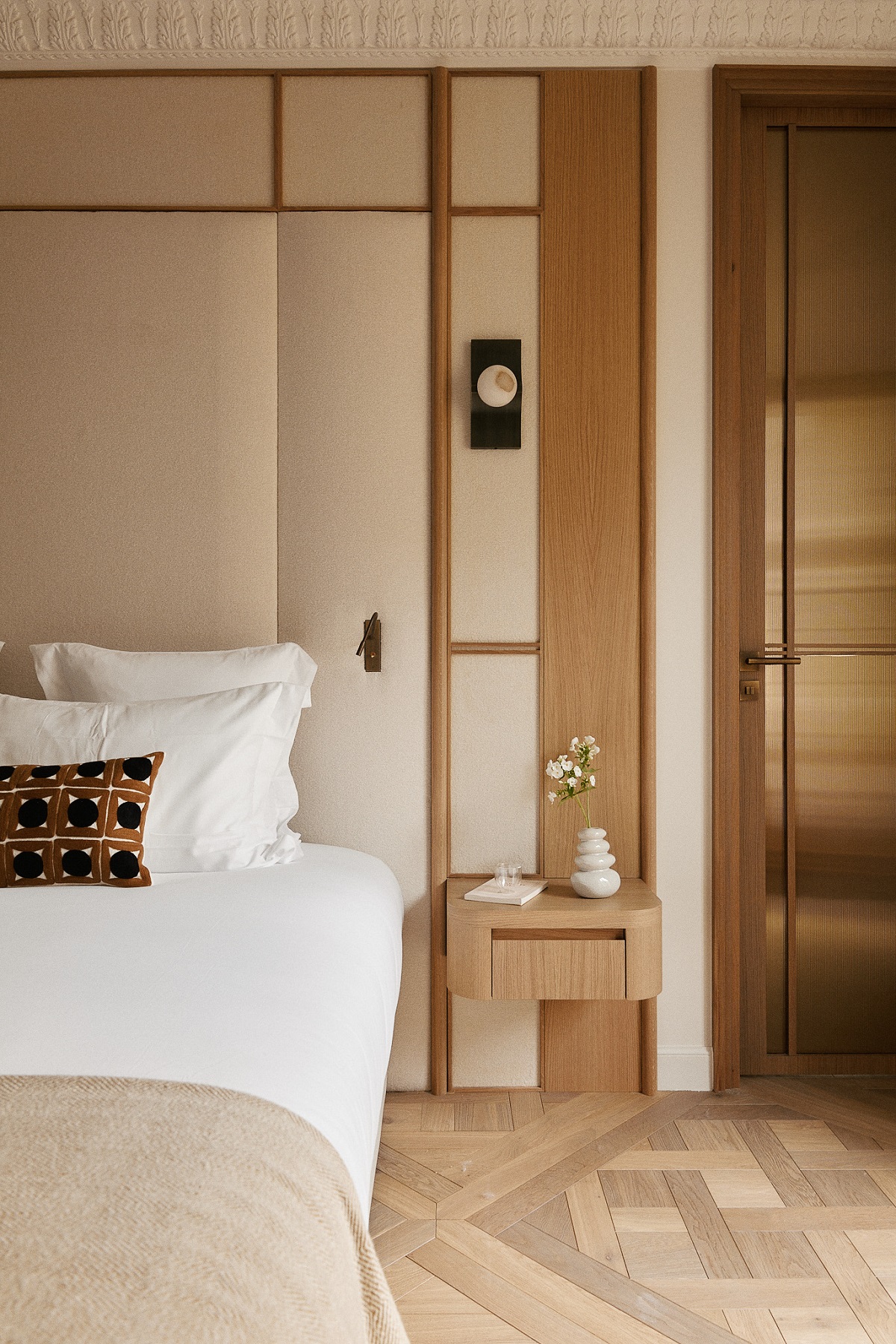 bedroom detail with white linen, patterned cushion and wood surfaces