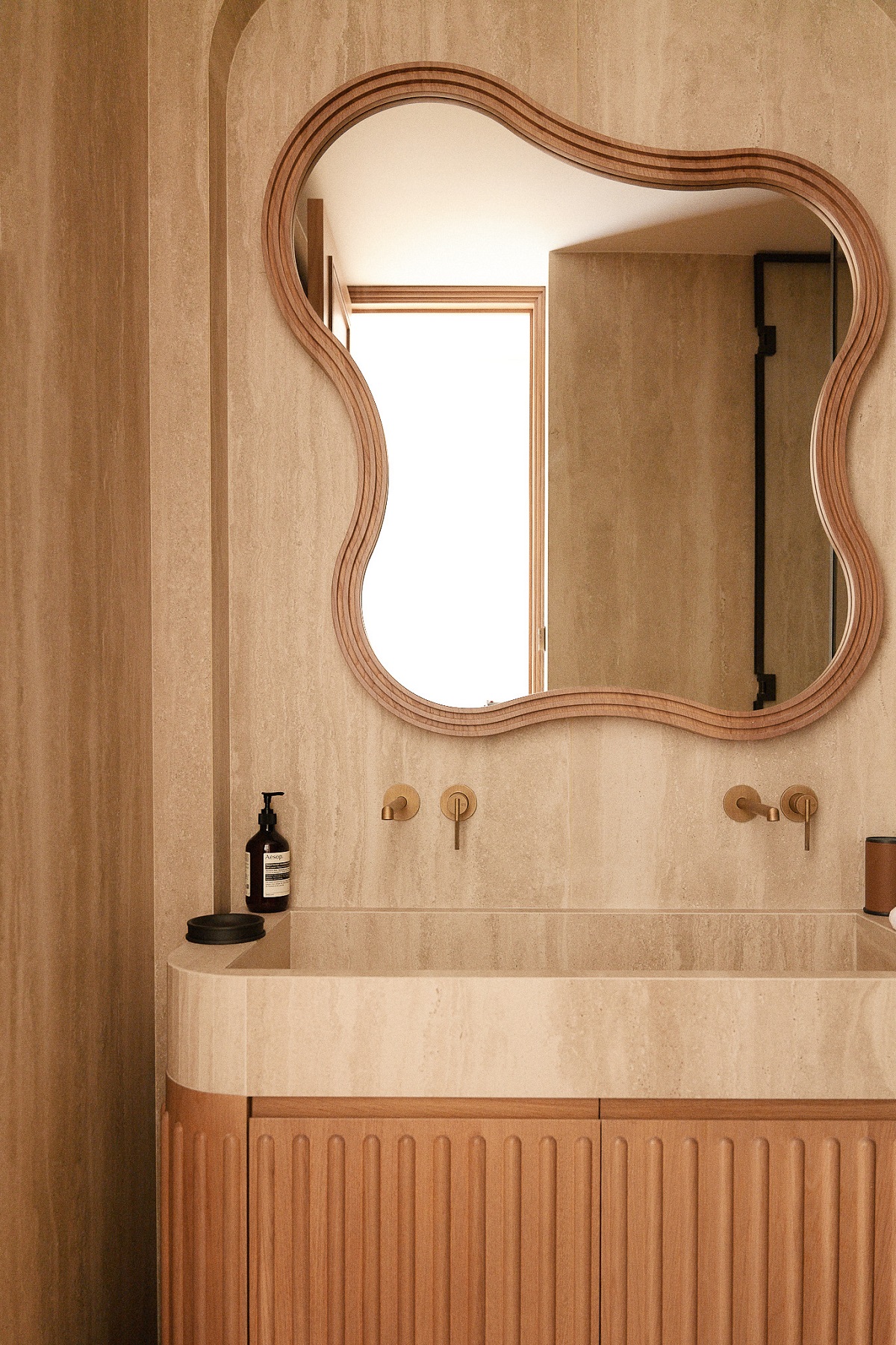organic shaped bathroom mirror above marble and wood vanity