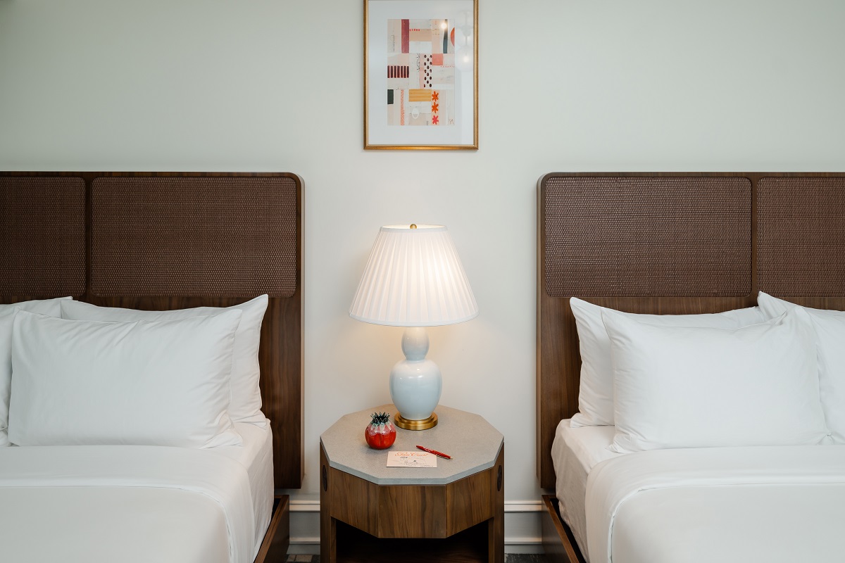 detail of 2 beds in guestroom with table, lamp and art on wall between