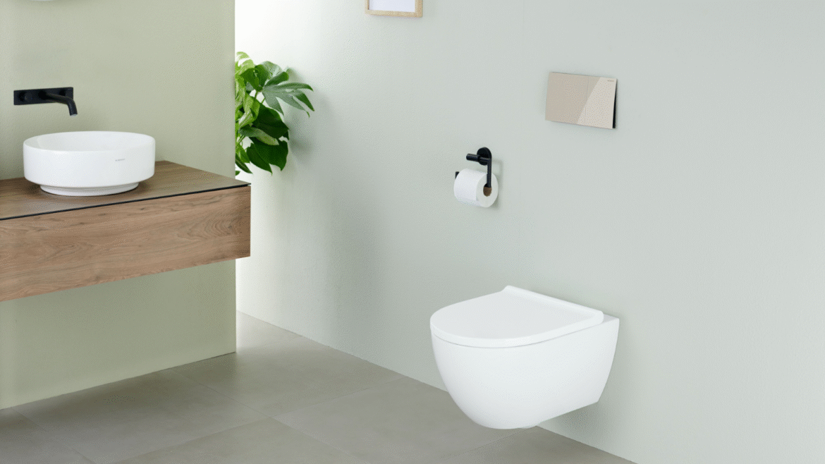 Geberit shower toilet mounted onto pale green wall, a chrome flush plate sits above