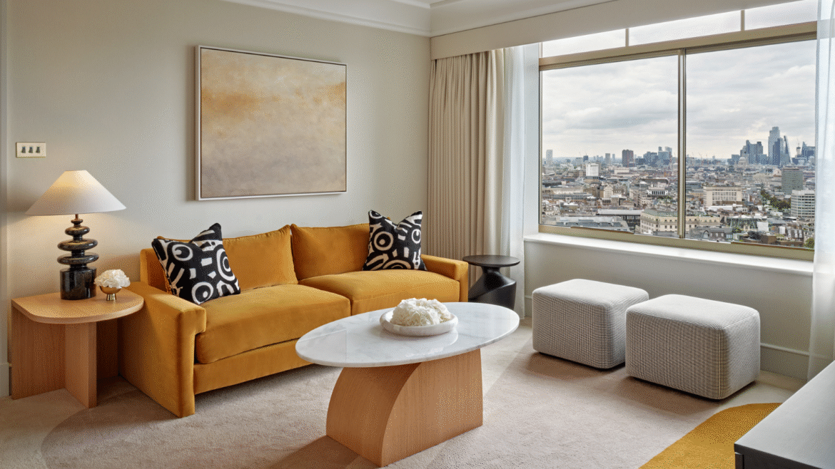 Lounge area in guest bedroom of Hilton Park Lane. Large window shows views across London while a yellow sofa is positioned besides a side table with Northern Lights ceramic lamp