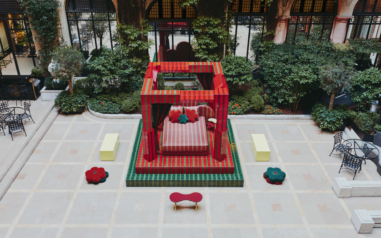 Raised on a platform and framed by bold red and green pillars, the ‘Day Bed’ structure feels at once playful and monumental. A fusion of sharp lines and organic shapes, the installation is industrial yet sumptuous. Low stools and benches in bright, Crayola hues are scattered across the tiled courtyard, inviting visitors to pause and take in the scene. With its bold palette of Plaza red and garden green, Uchronia has transformed the Hôtel Plaza Athénée courtyard space into a contemporary cubist exhibition, where – like a strange dream – a geometric bed awaits sleep outside, encased within the white walls of historic Paris.
