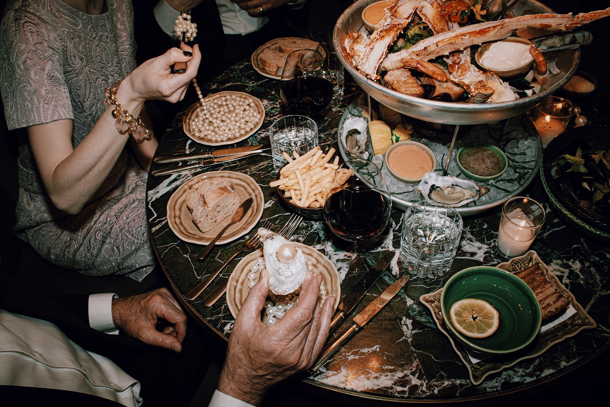 birds eye view of dinner table and hands with oysters and eating a string of pearls