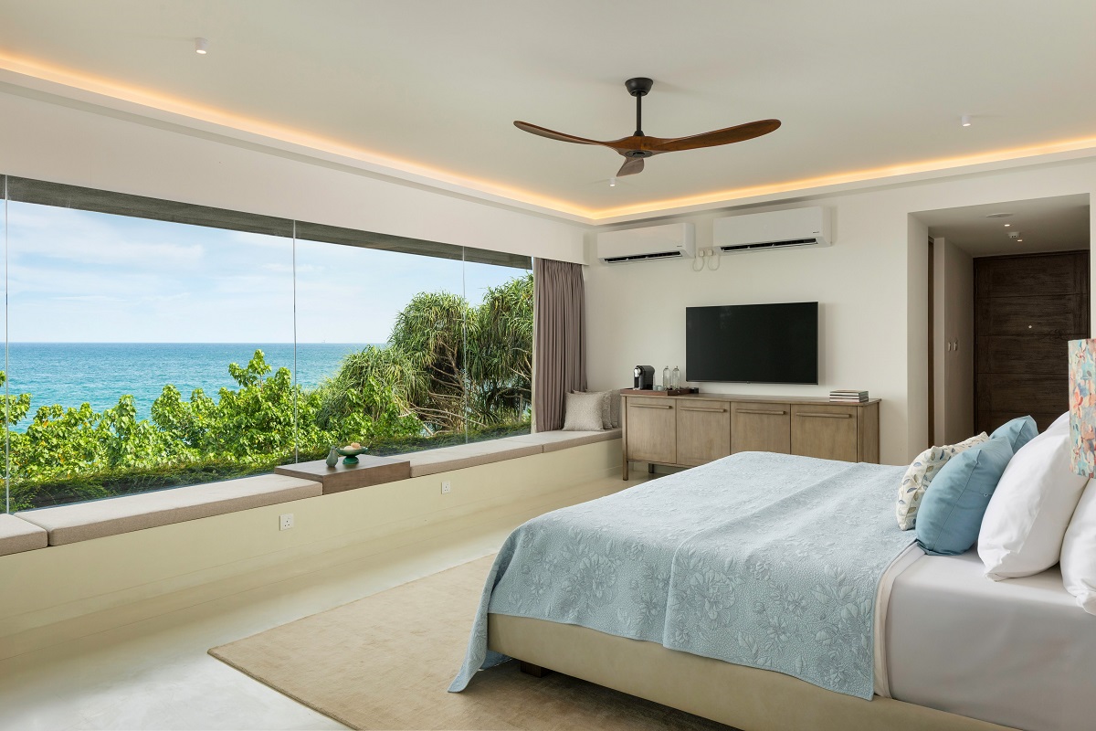 bed in hotel guestroom with large window with seaview in front of it