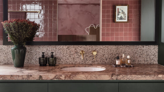 Red/pink stone bathroom with dark green walls and brass tap by ABI Interiors