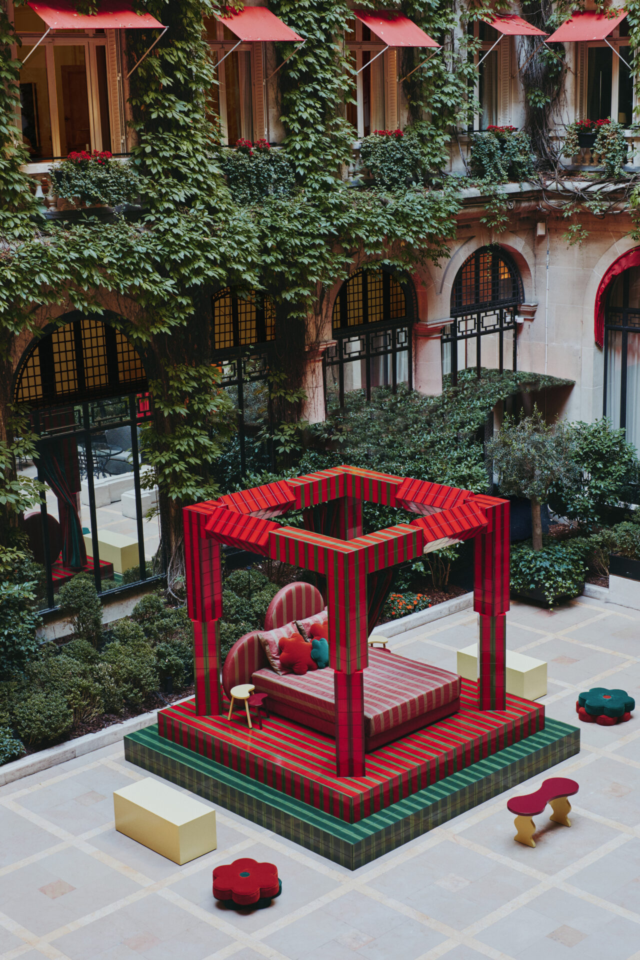 Raised on a platform and framed by bold red and green pillars, the ‘Day Bed’ structure feels at once playful and monumental. A fusion of sharp lines and organic shapes, the installation is industrial yet sumptuous. Low stools and benches in bright, Crayola hues are scattered across the tiled courtyard, inviting visitors to pause and take in the scene. With its bold palette of Plaza red and garden green, Uchronia has transformed the Hôtel Plaza Athénée courtyard space into a contemporary cubist exhibition, where – like a strange dream – a geometric bed awaits sleep outside, encased within the white walls of historic Paris. contemporary art installation in Paris