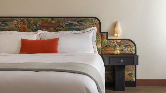 detail of bed with white linen, orange cushion and mid century design upholstered bedhead in Hotel Daphne from Bunkhouse
