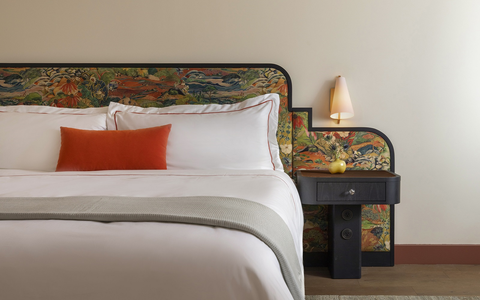 detail of bed with white linen, orange cushion and mid century design upholstered bedhead in Hotel Daphne from Bunkhouse