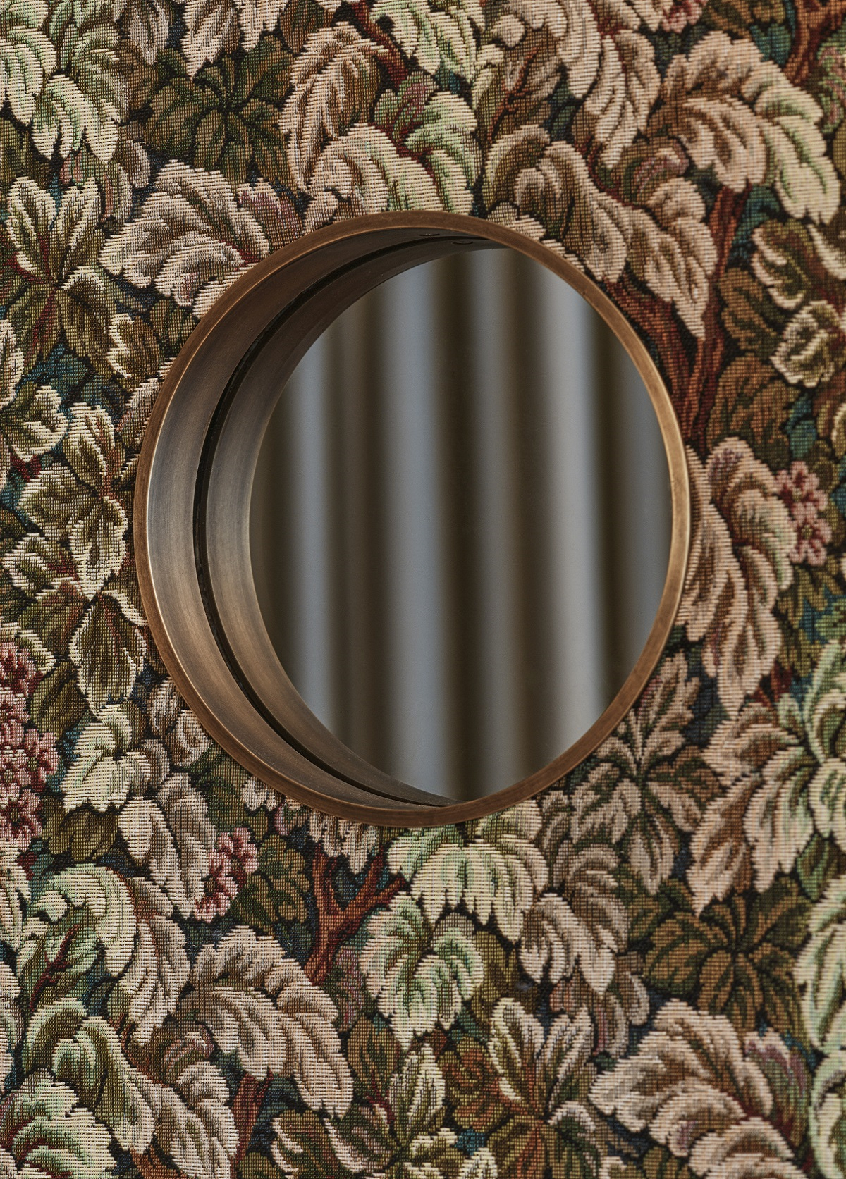 floral wallpaper in olive green surrounding a round mirror detail