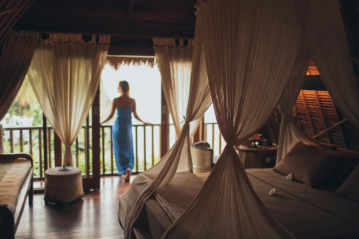 woman in sarong standing in front of draped curtains on guestroom balcony